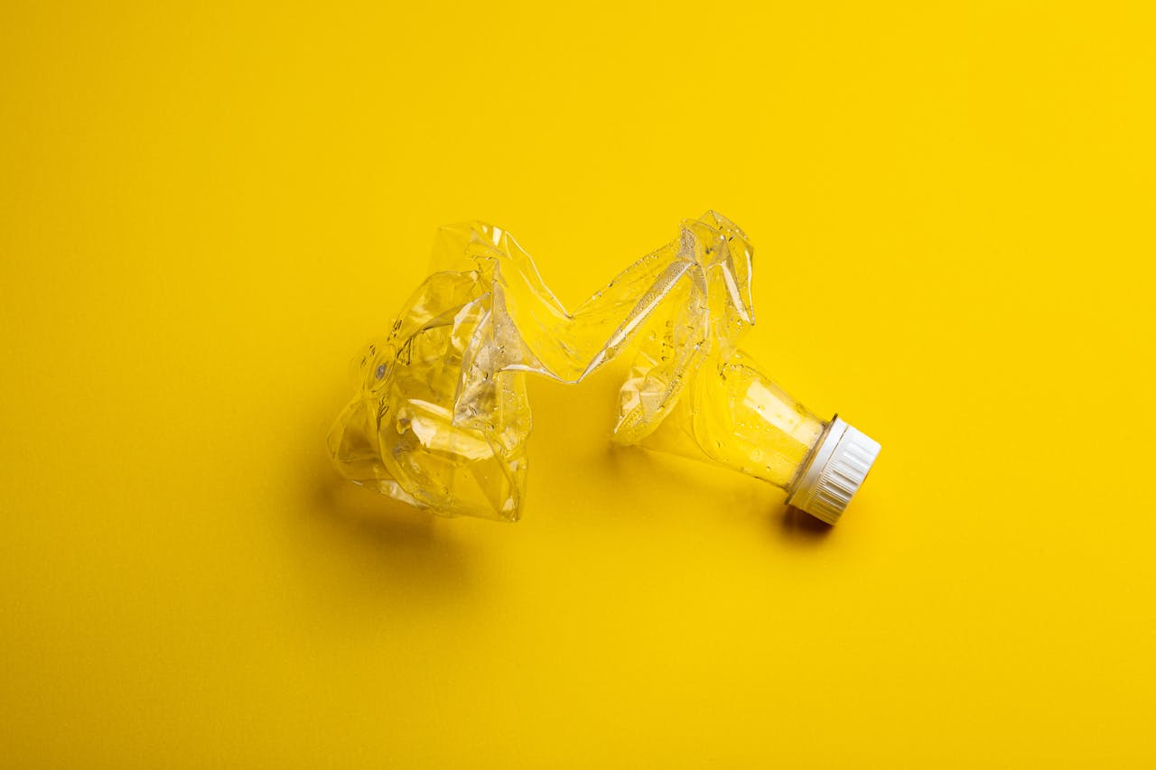 A crumpled plastic bottle against a bright yellow backdrop, highlighting recycling themes.